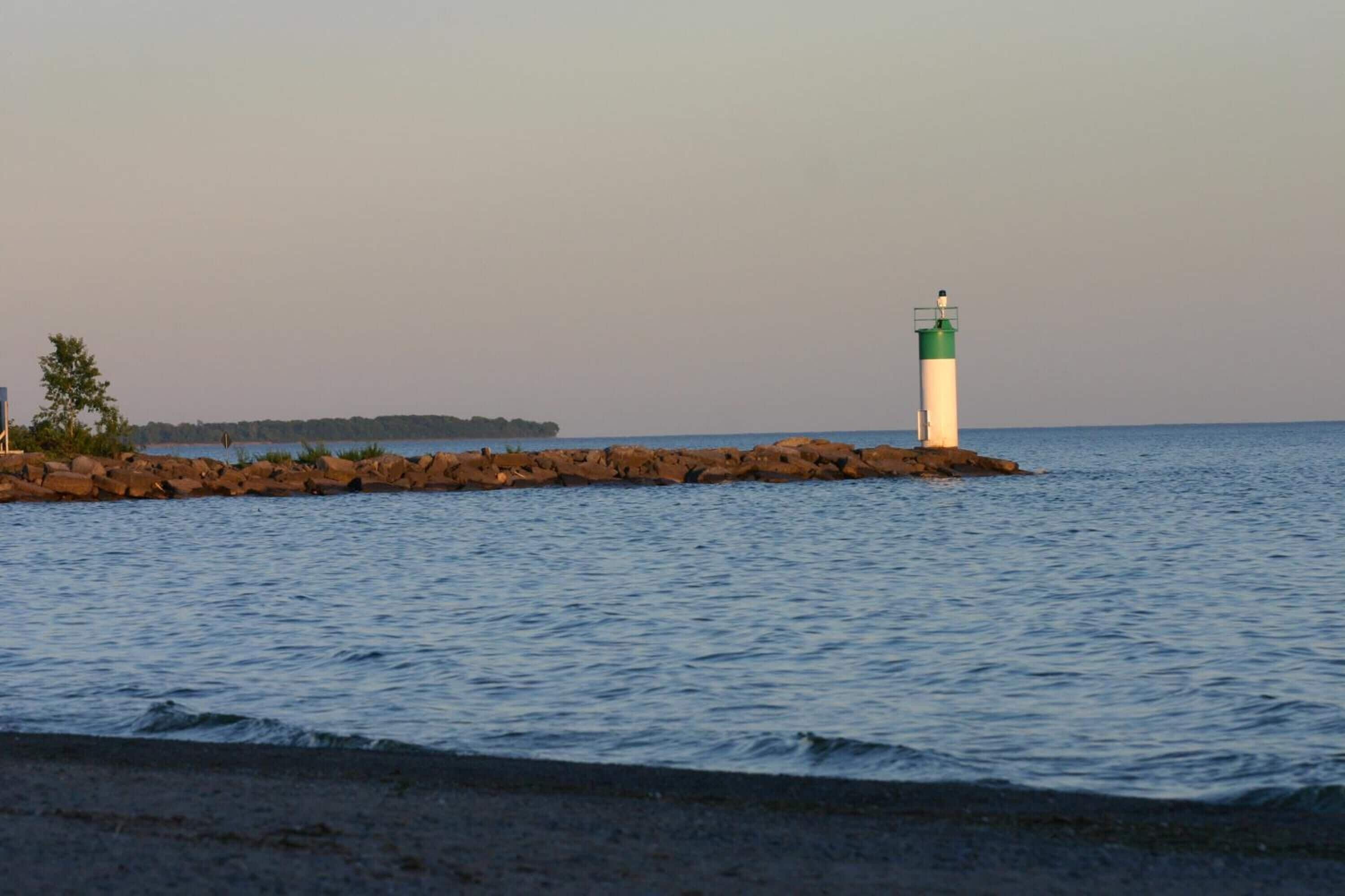 Un faro sobre un afloramiento rocoso, con aguas tranquilas y una costa lejana.