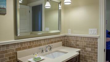 A bathroom with a beige sink, two faucets, a large mirror, and a light fixture above.