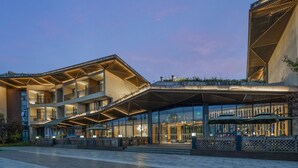A modern hotel with a multi-story structure, large glass windows, and outdoor seating areas. - Holiday Inn Express Emei Mountain by IHG (Leshan)