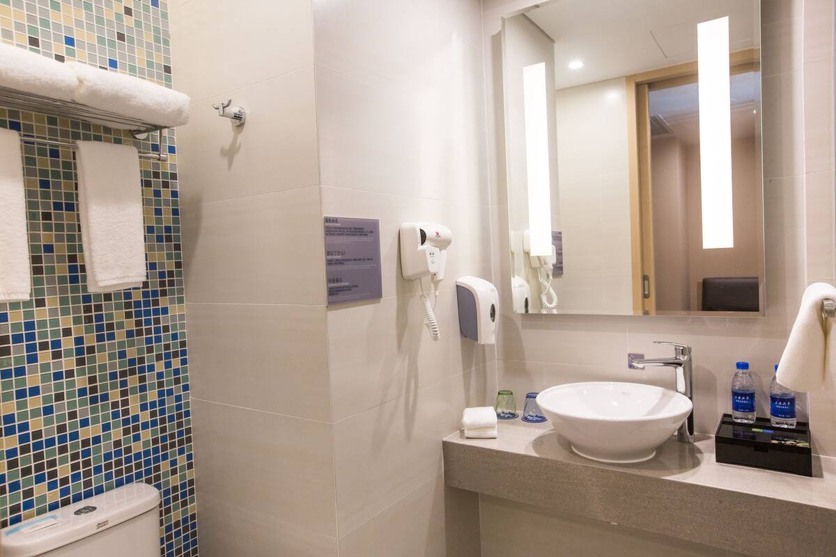 A bathroom with a tiled wall, a sink, a mirror, a towel rack, and a toilet.