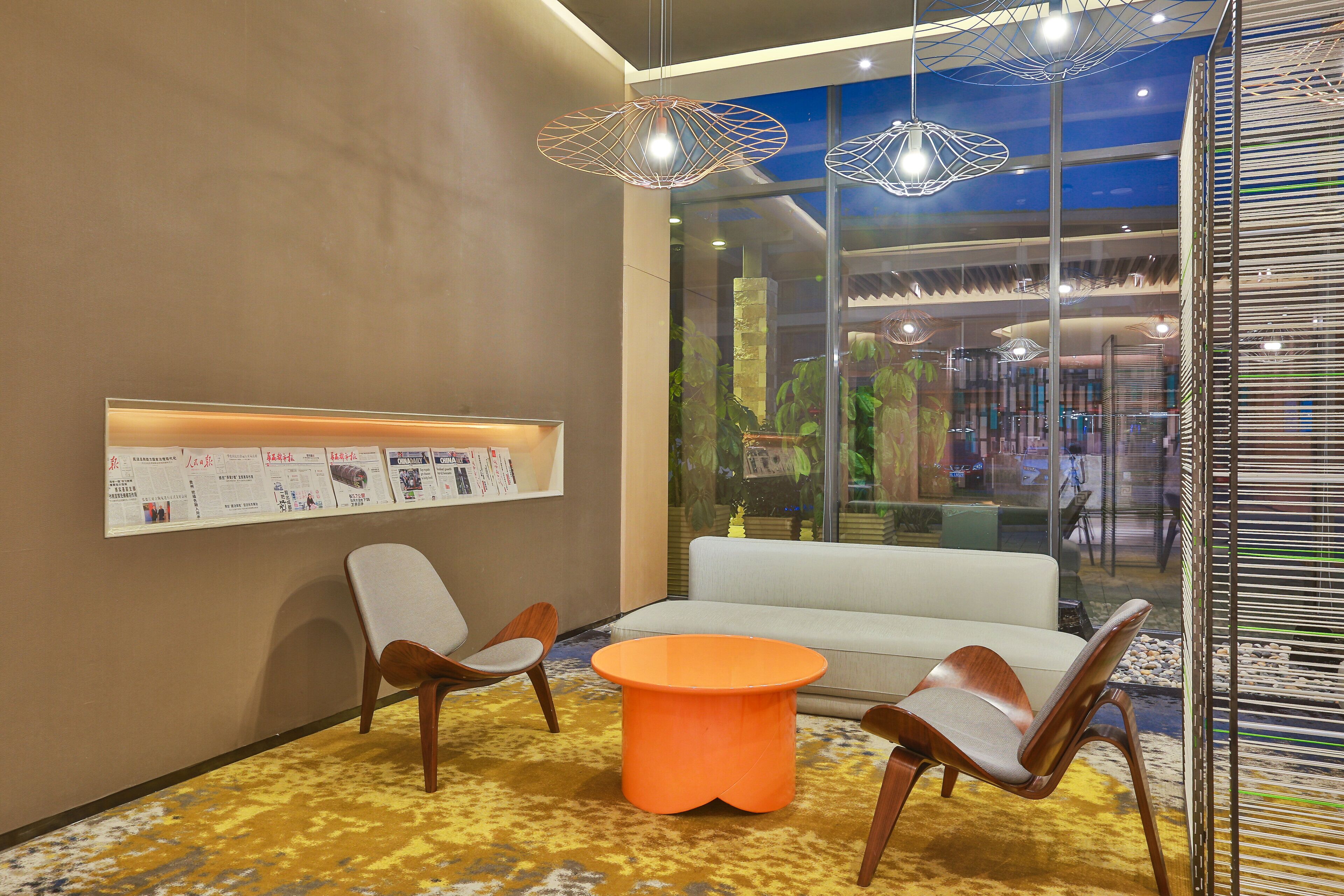 Un interior moderno con una mesa redonda naranja, dos sillas de madera, un sofá blanco y lámparas colgantes.