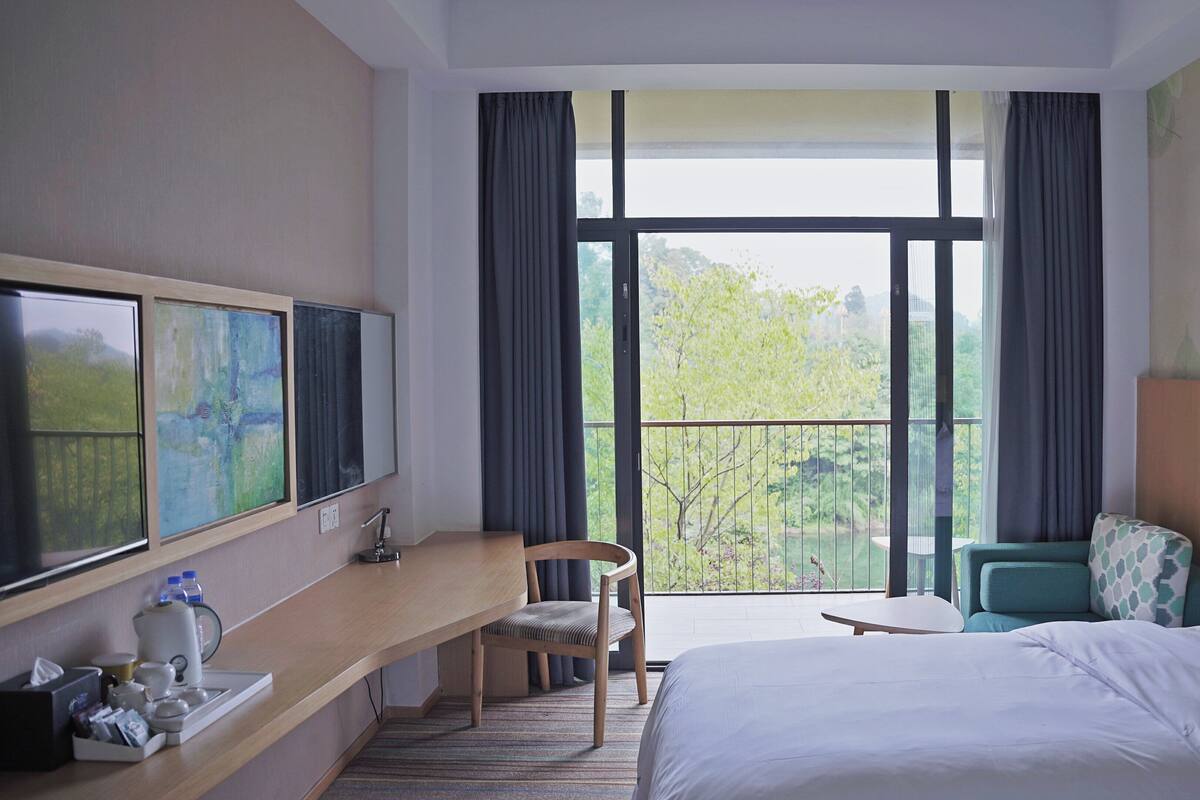 A hotel room with a bed, a desk, a chair, a small table, and a TV.