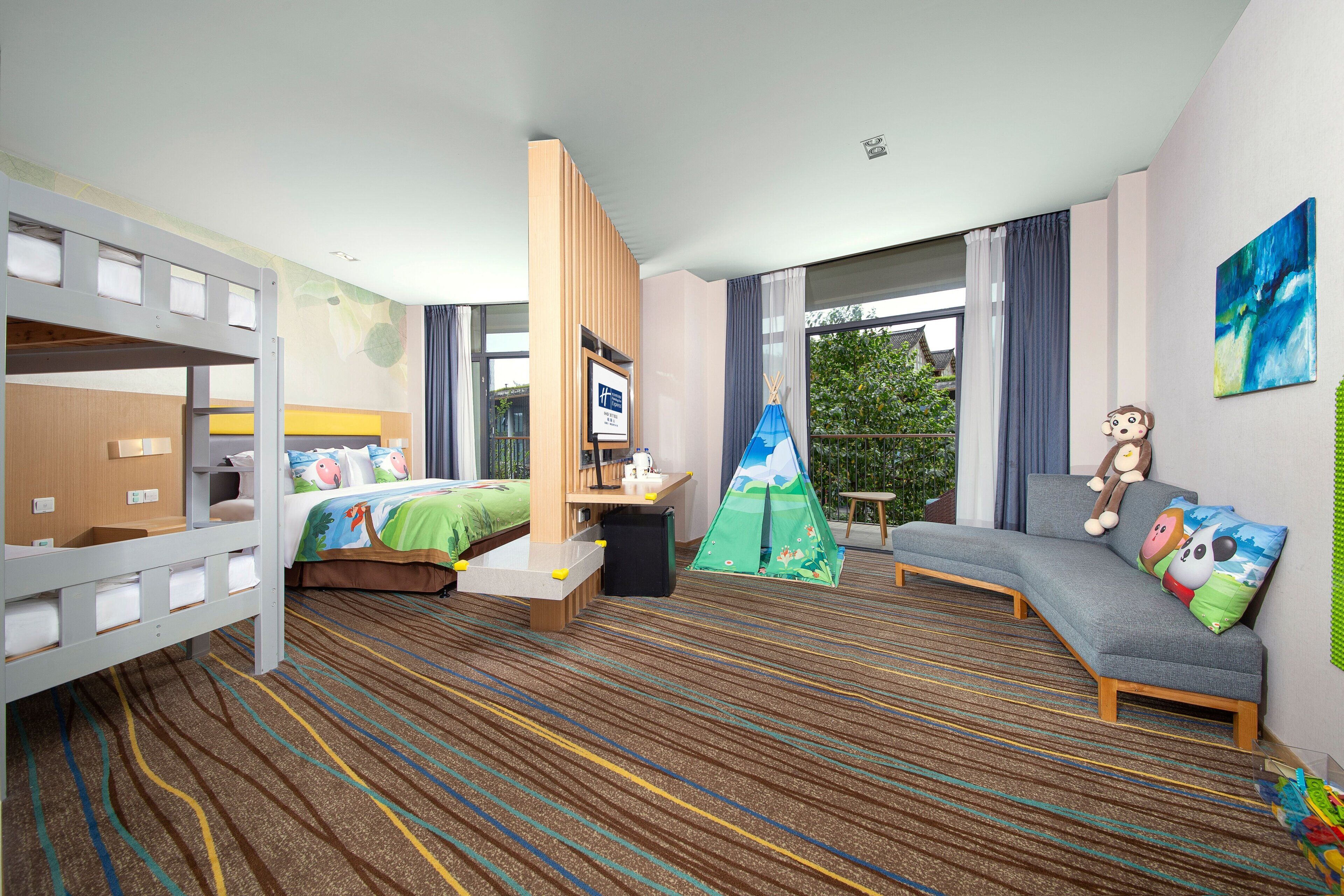 Ein Hotelzimmer mit Etagenbett, einer Schlafcouch, einem kleinen Tisch und einer zeltartigen Spielecke.