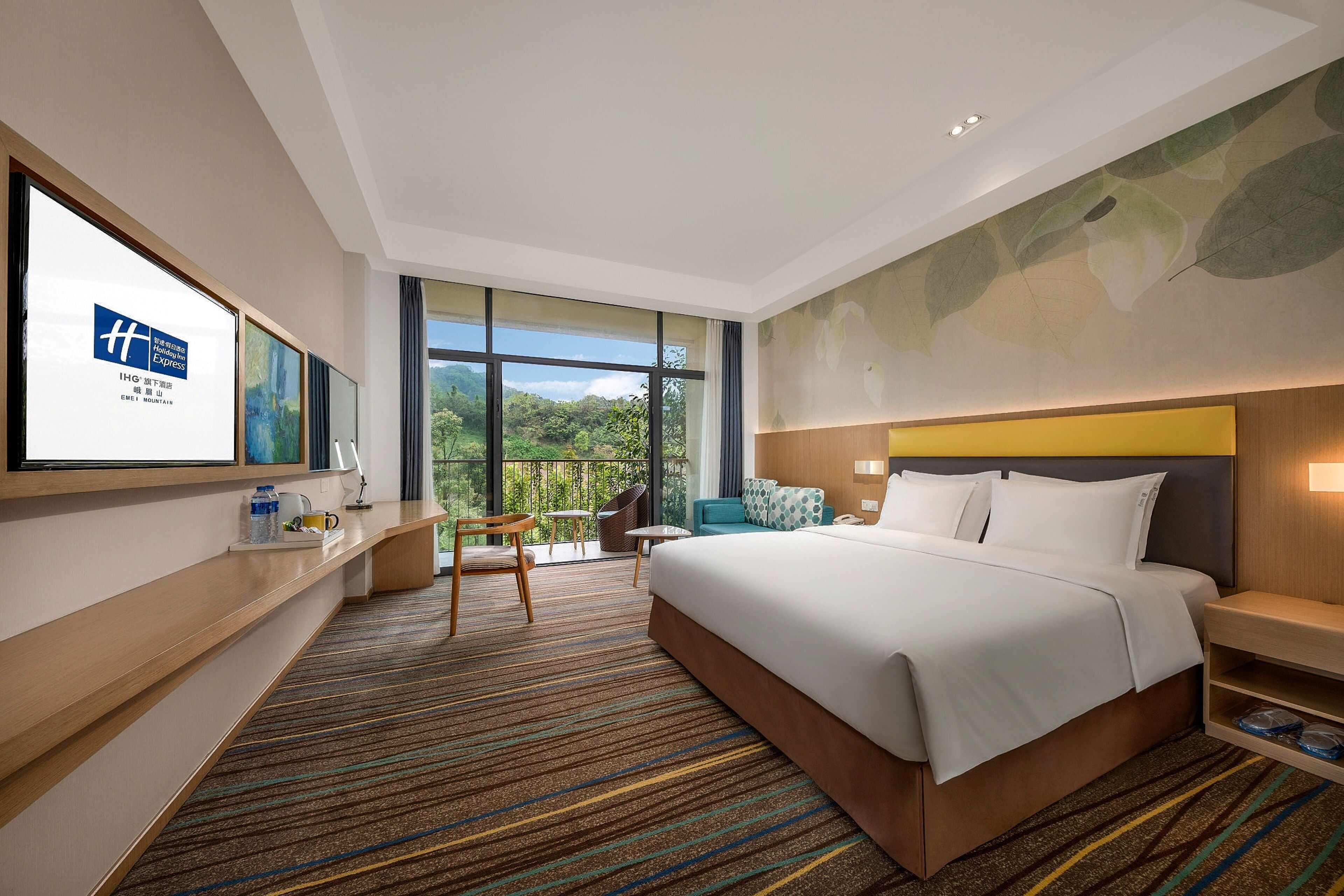 A hotel room with a large bed, a desk, a chair, a small table, and a view of the outdoors.