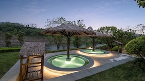 A serene outdoor area with thatched umbrellas, circular water features, and a wooden bench. - Holiday Inn Express Emei Mountain by IHG (Leshan)