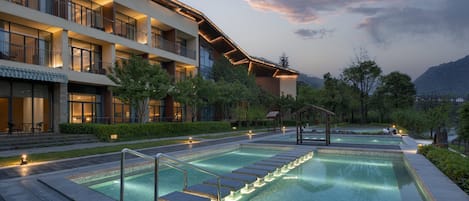 A hotel with a swimming pool, outdoor seating, and a view of the mountains.