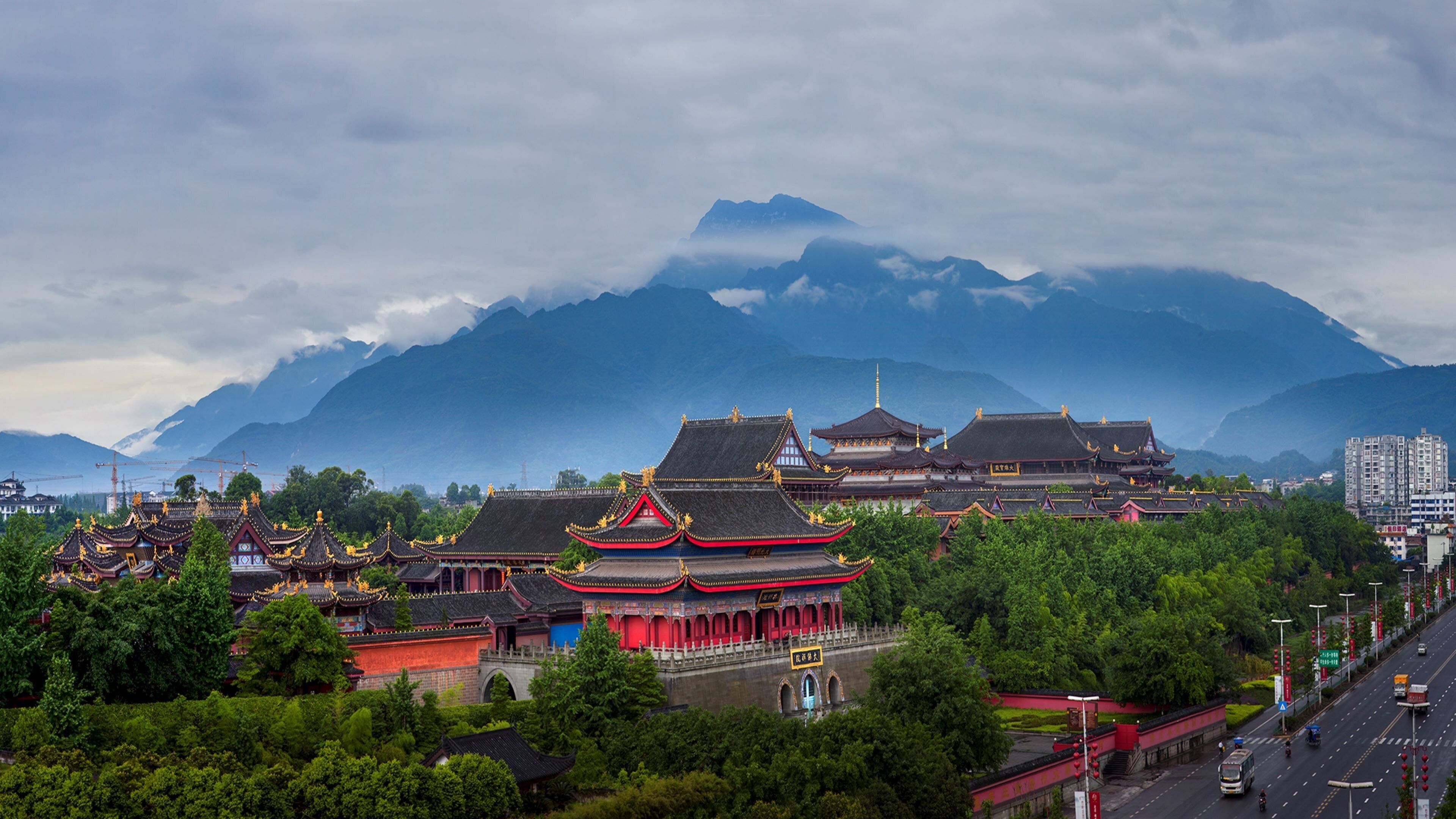 A traditional Chinese architectural complex with multiple buildings, a bridge, and a mountainous backdrop.