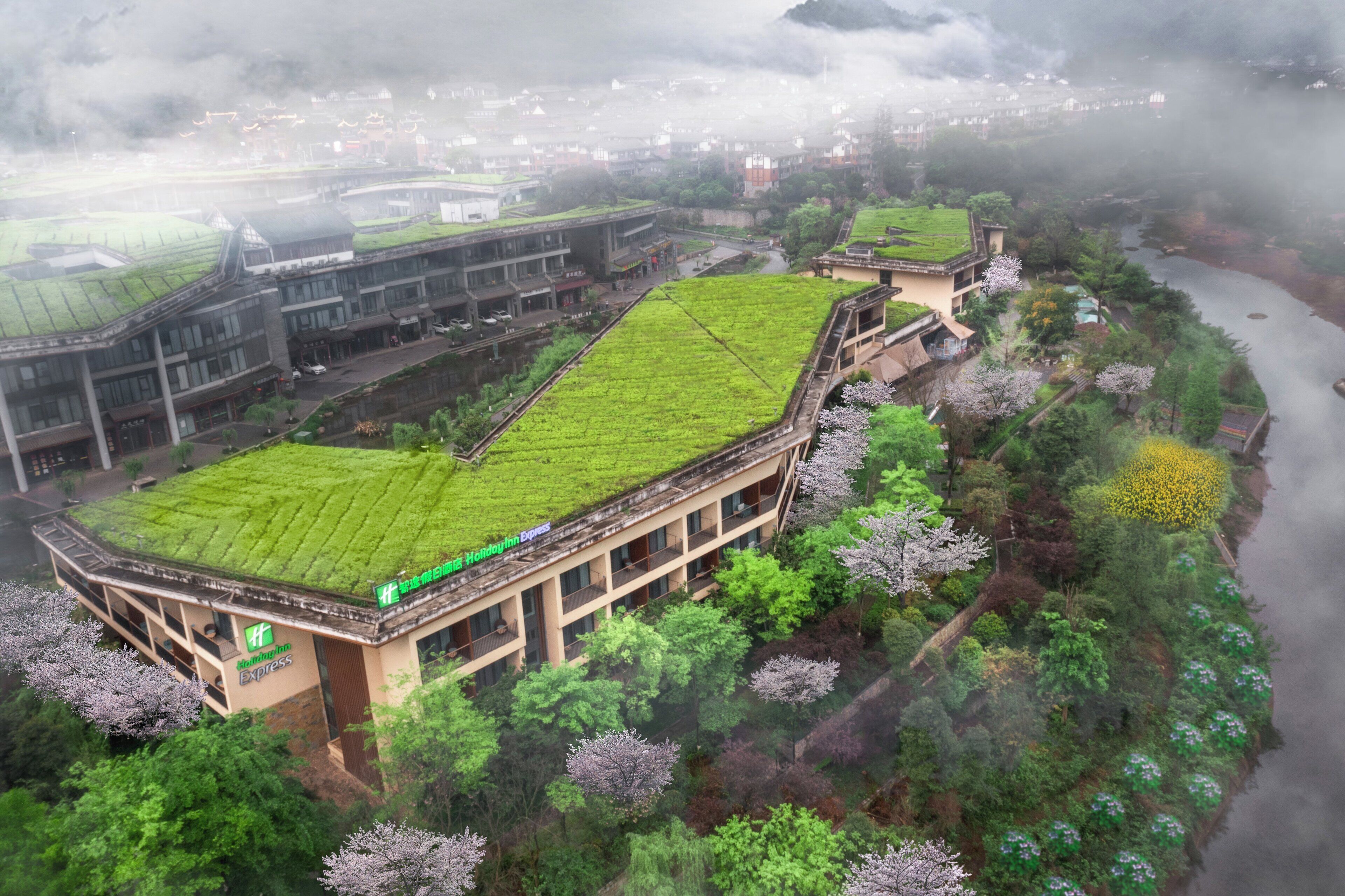A hotel with a green roof, surrounded by lush greenery and a river.