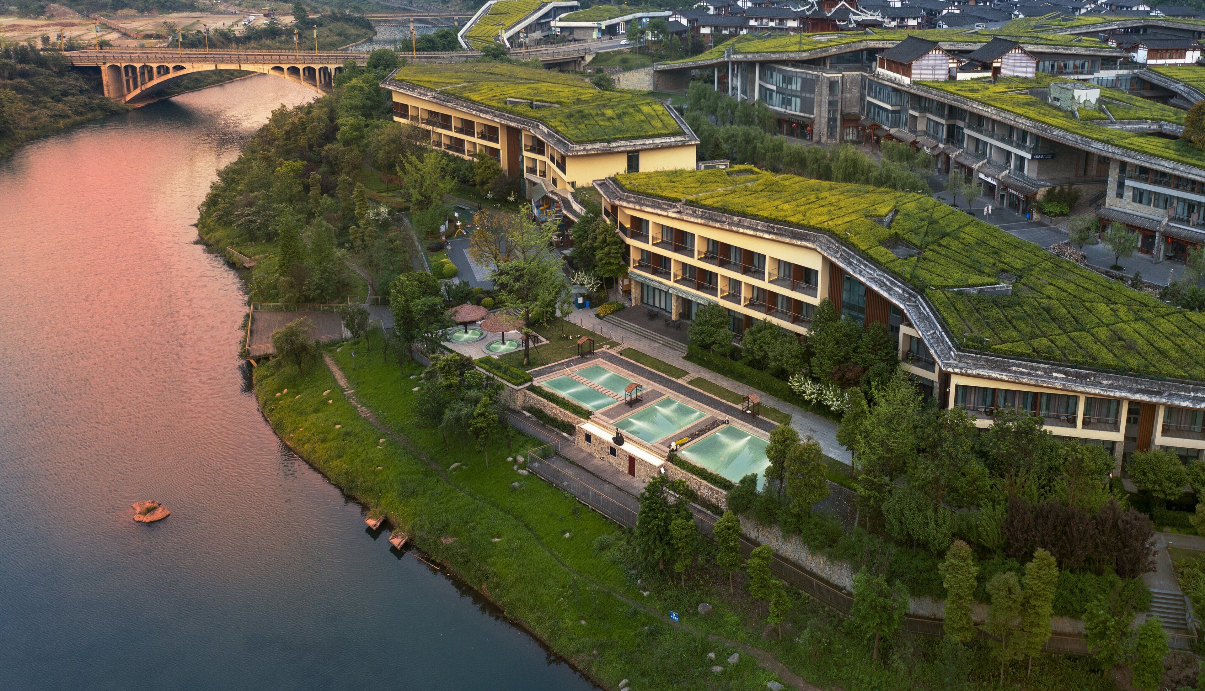 A modern building with green roofs, a river, and a bridge.