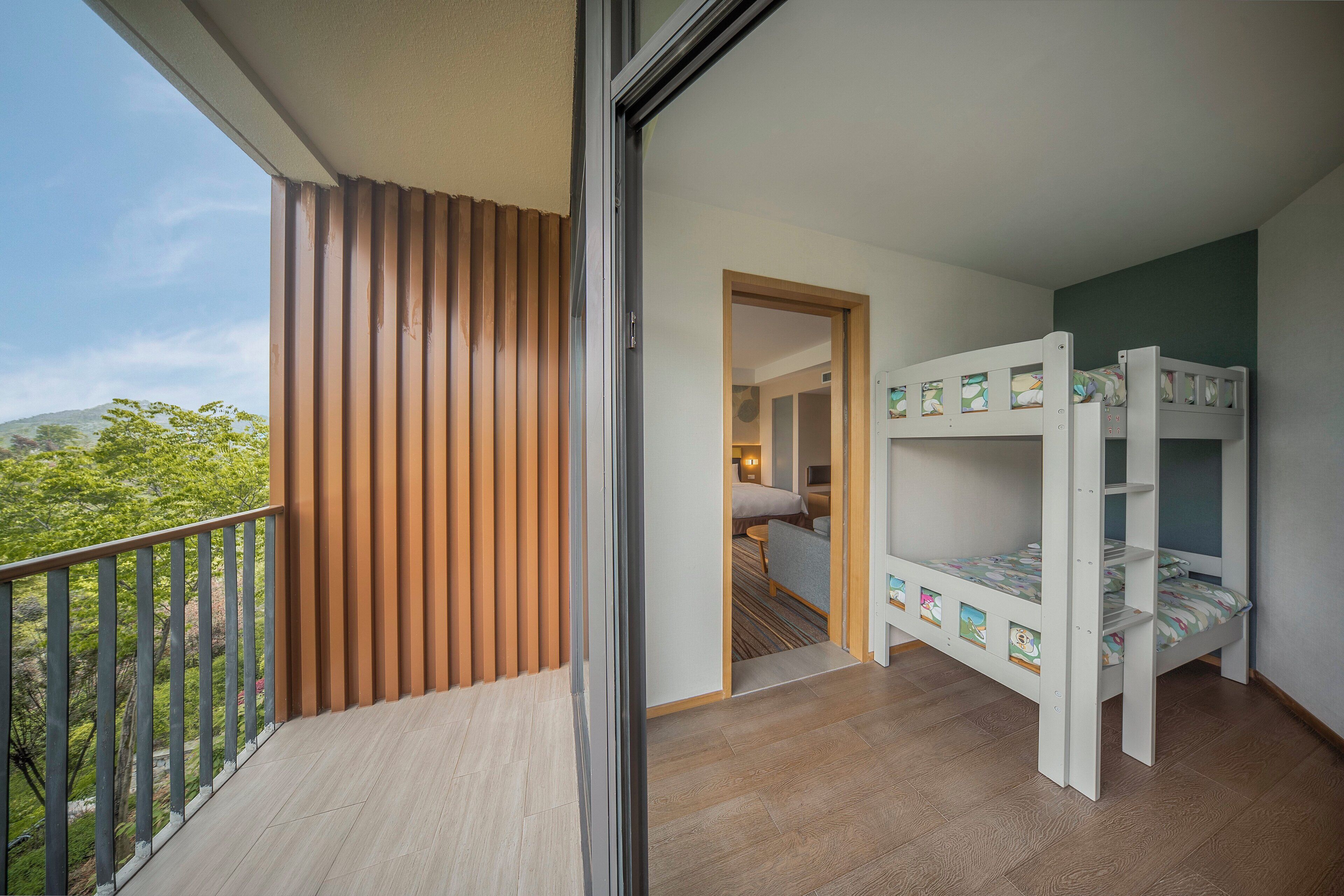A balcony with a wooden slat design and a view of greenery. A bunk bed with colorful bedding is visible in the room.
