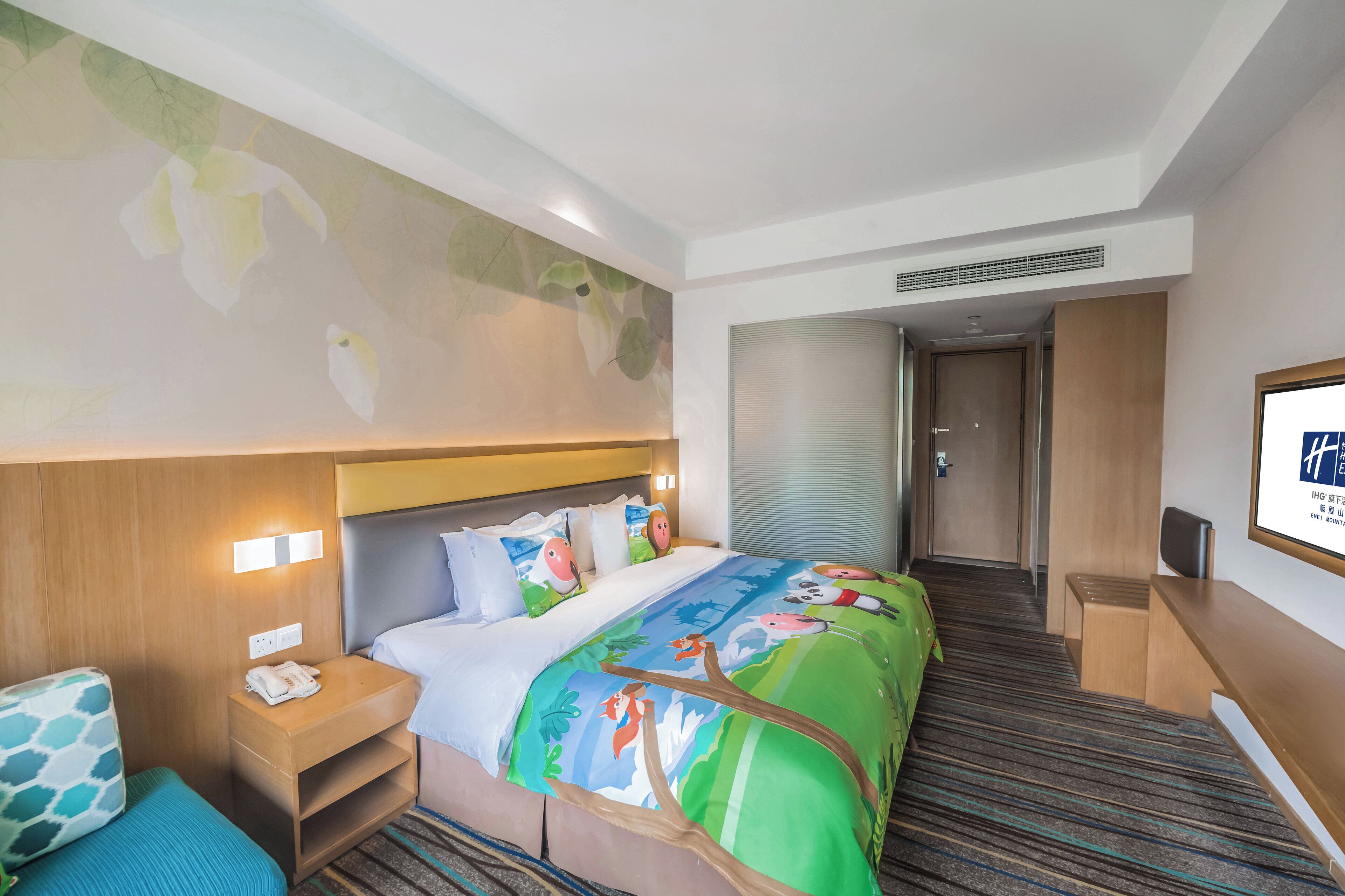 Ein Hotelzimmer mit Bett, Nachttisch, Schreibtisch und einem an der Wand montierten Fernseher.