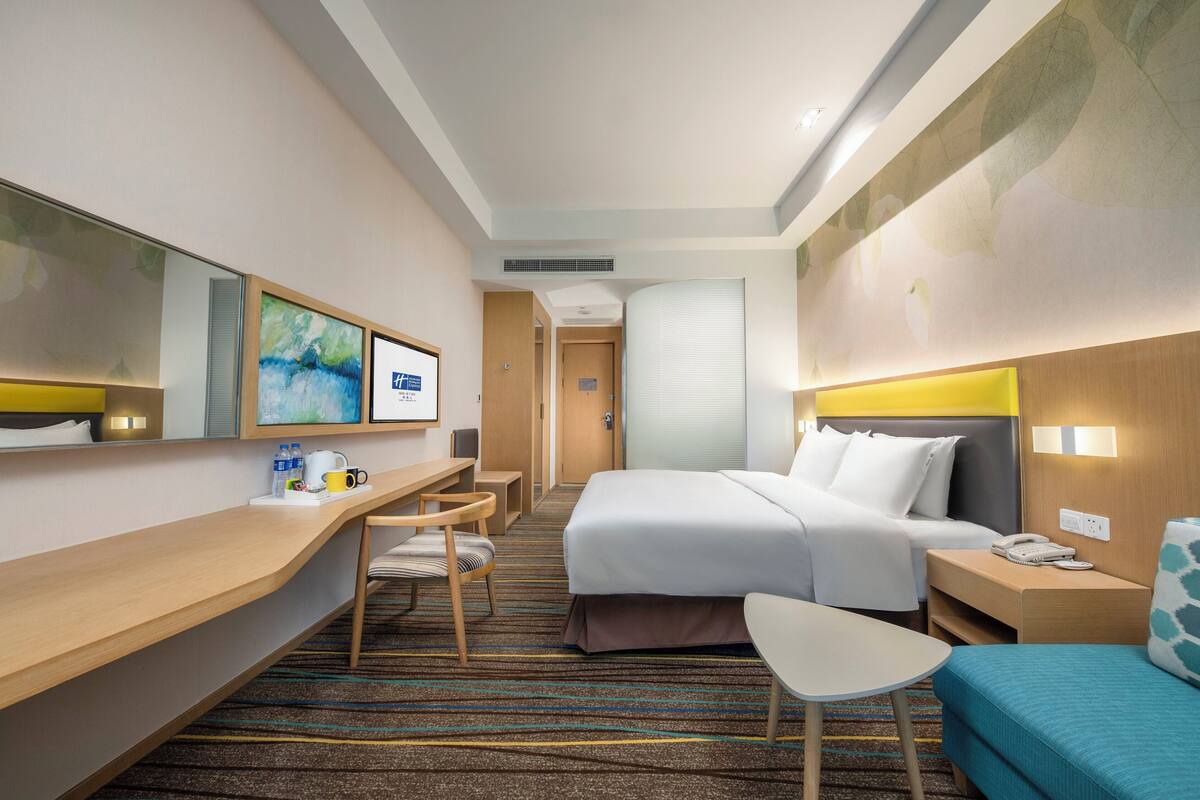 A hotel room with a bed, bedside table, chair, desk, and a large mirror.