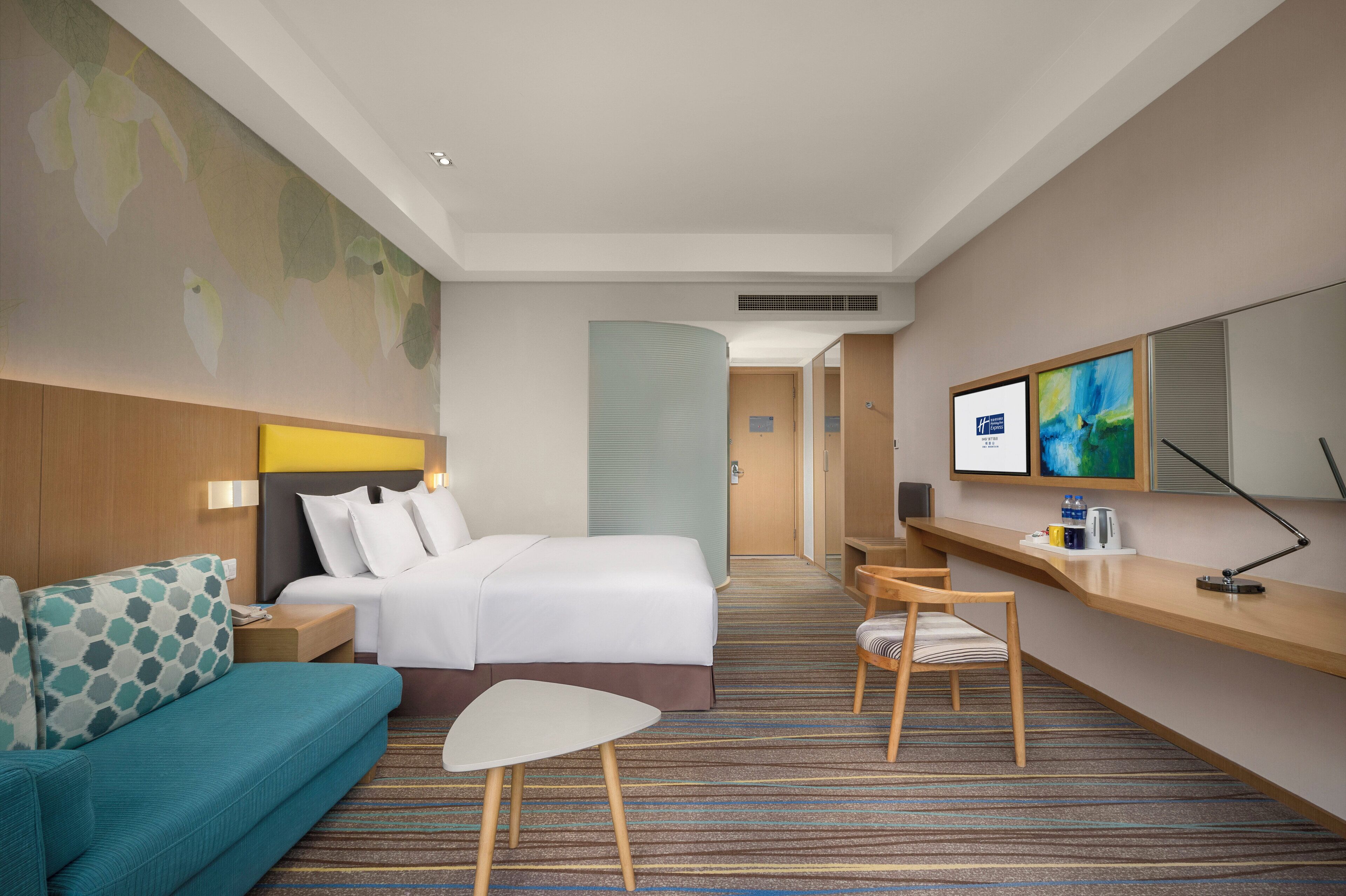 A hotel room with a bed, a sofa, a desk, a chair, a TV, and a large window.