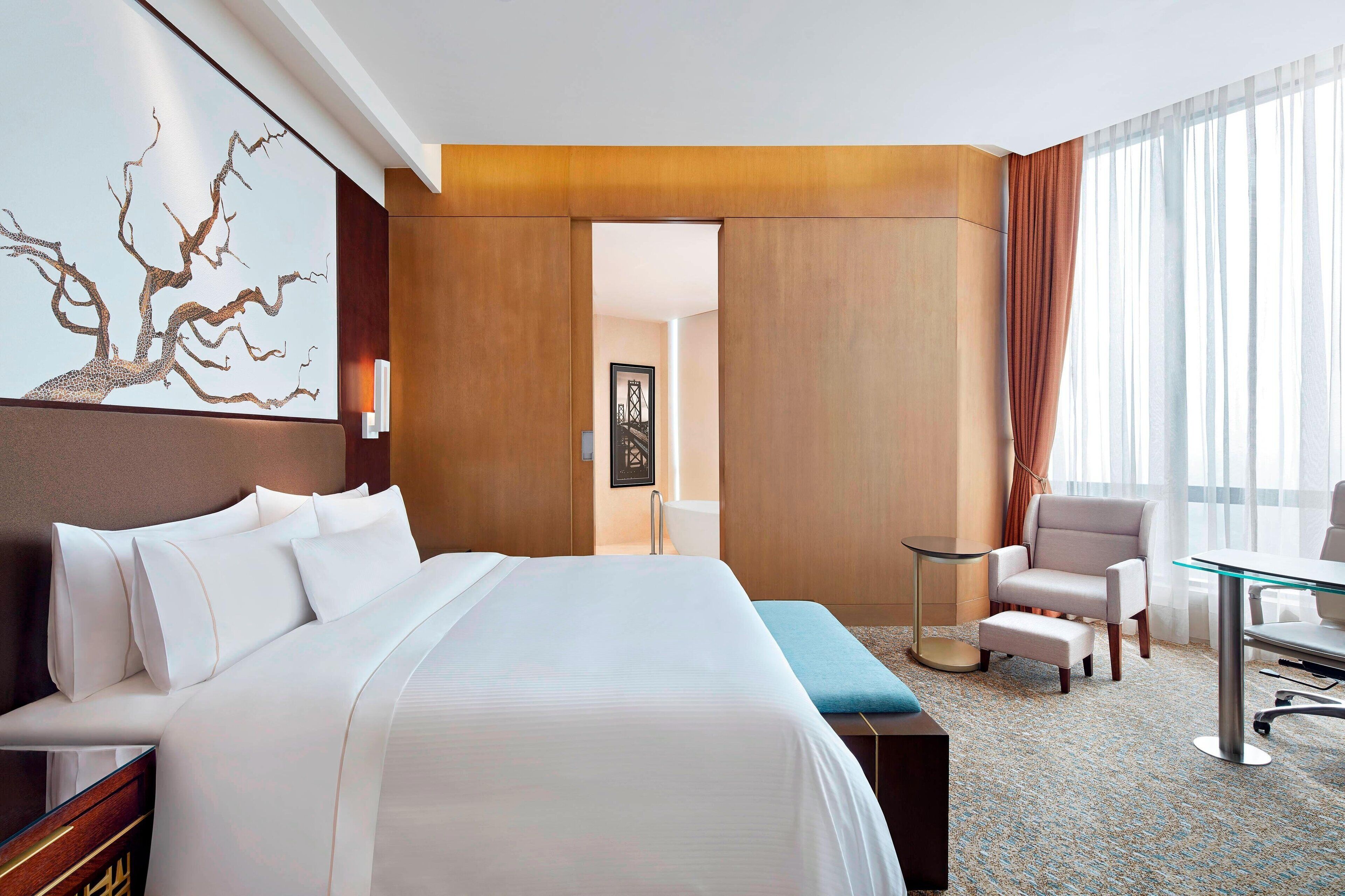 Quarto de hotel com cama grande, escrivaninha, cadeira e vista para a cidade pela janela.