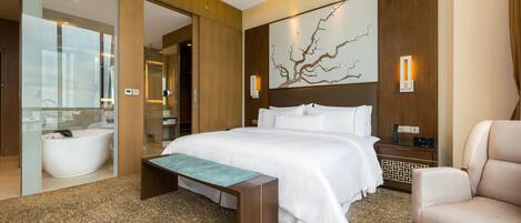 Habitación de hotel moderna con una cama grande, un banco, una silla, una bañera y una obra de arte colgada en la pared.