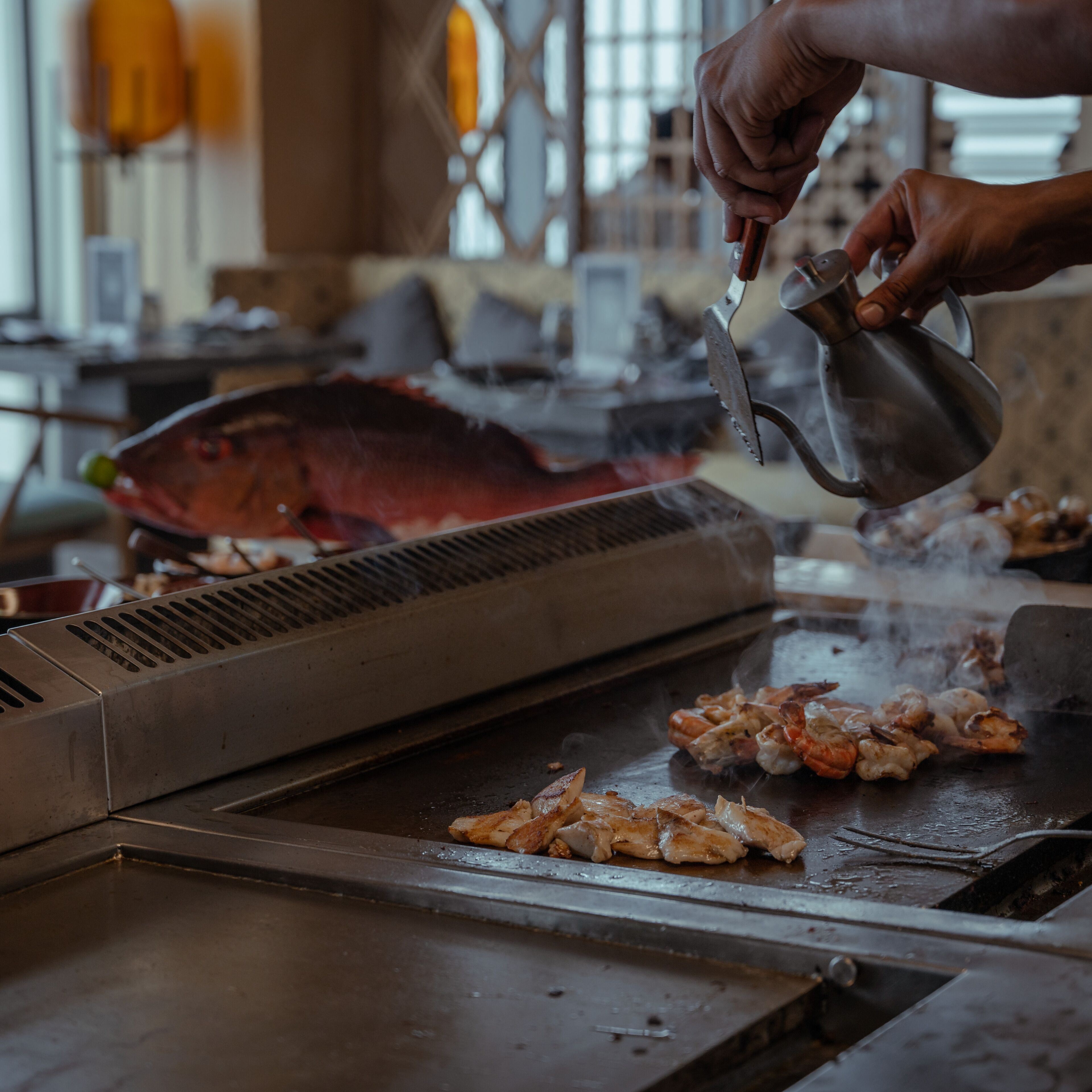 A person grilling seafood on a flat-top grill with steam rising.