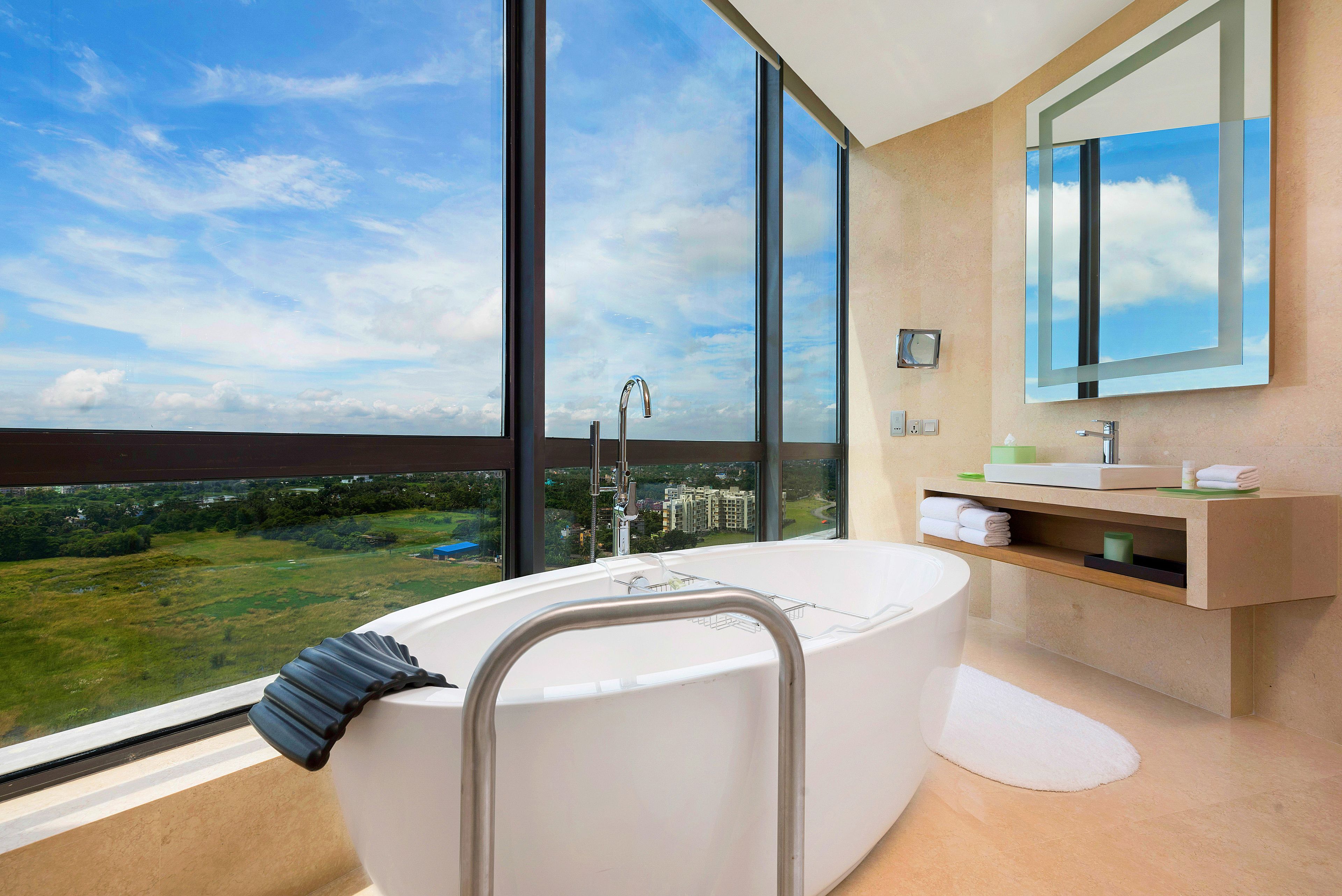 A modern bathroom with a large bathtub, a vanity with a mirror, and a view of a green landscape through large windows.