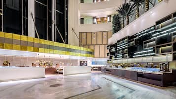 Un vaste atrium doté d’un haut plafond, avec un îlot central où sont exposés des objets, entouré d’espaces de détente et d’un escalier moderne.