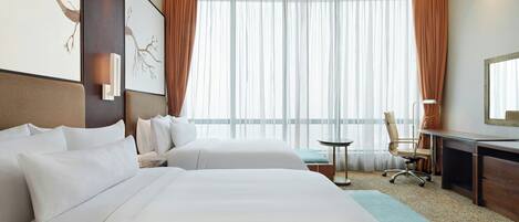 Camera d'albergo con due letti, una scrivania, una sedia, un tavolino e un'ampia finestra con tende.