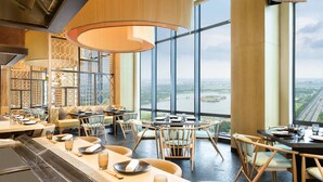 A modern restaurant with high ceilings, large windows, and a view of a river. - The Westin Kolkata Rajarhat (Barasat)