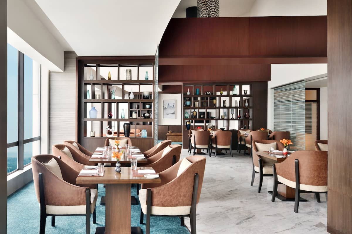 A modern dining area with a long table and multiple chairs, surrounded by a wooden bookshelf filled with decorative items.