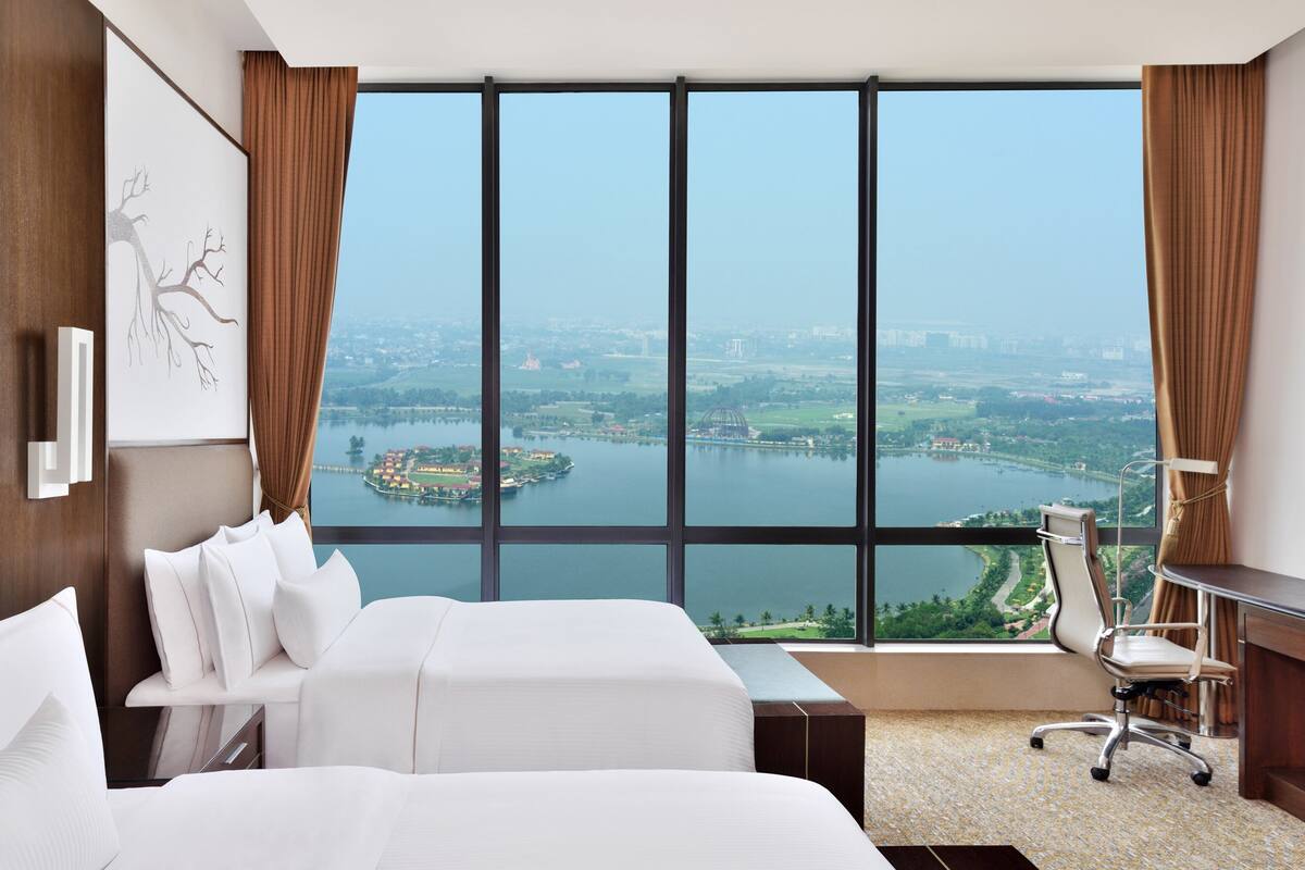 A hotel room with a large window offering a view of a lake and cityscape.