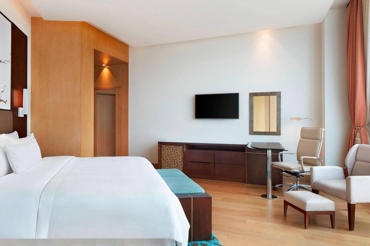 A hotel room with a large bed, a desk, a chair, and a television.