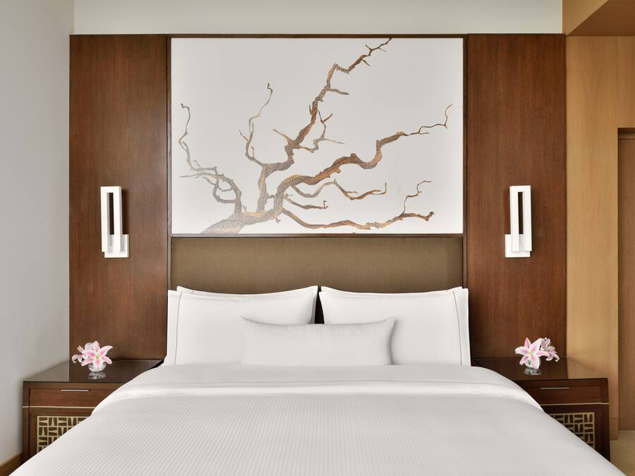 Una habitación de hotel moderna con una cama grande, un elemento decorativo en la pared y dos mesitas de noche con lámparas.