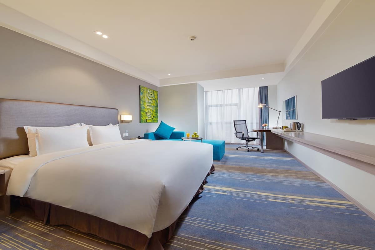 A hotel room with a large bed, a desk, a chair, a TV, and a window with curtains.