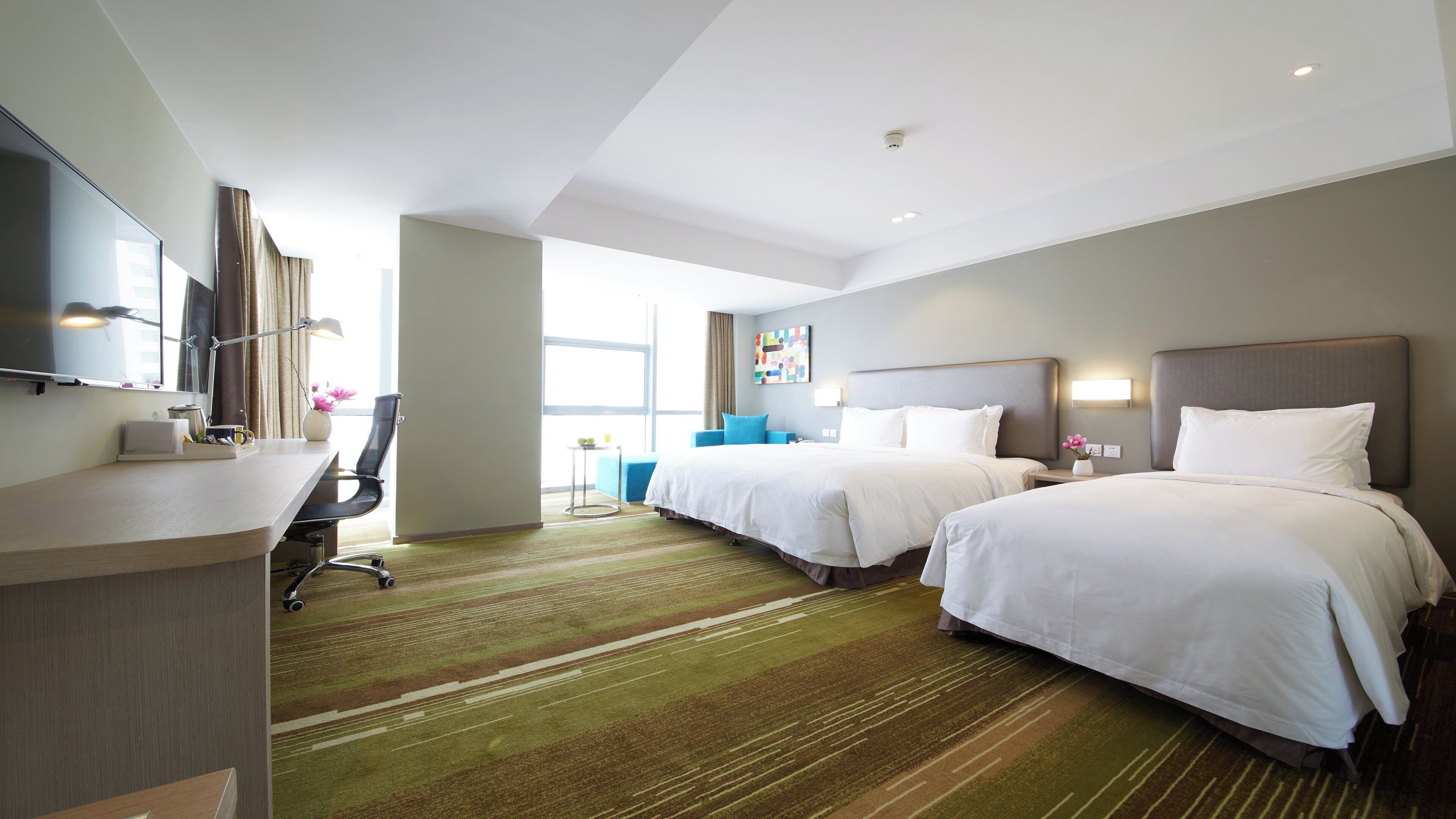 A hotel room with two beds, a desk with a chair, a flat-screen TV, and a large window.