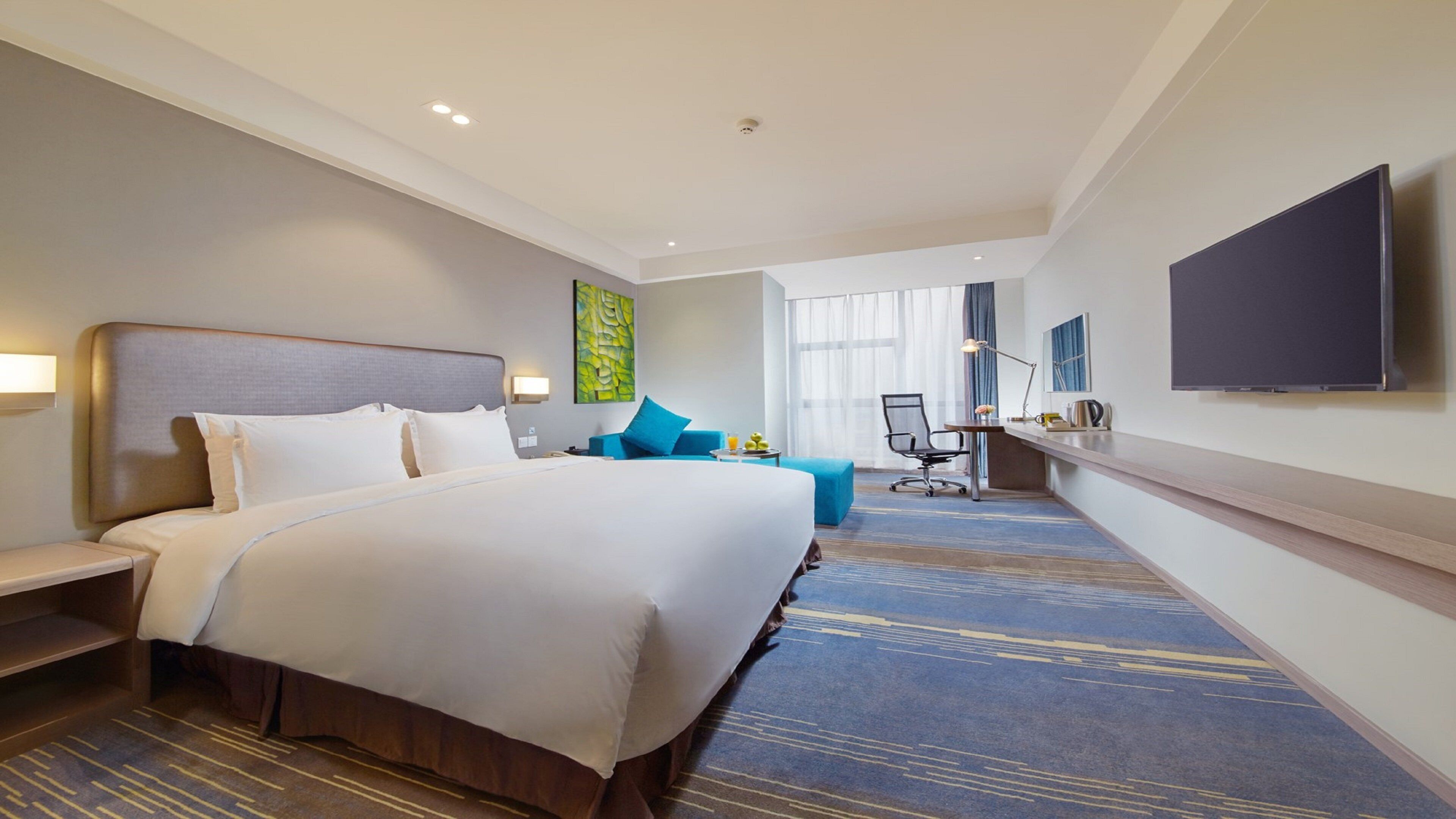 Quarto de hotel com uma cama grande, uma escrivaninha com cadeira, televisão de tela plana e janela com cortinas.