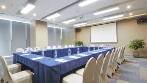A conference room with a long table, chairs, water bottles, a projector screen, and a potted plant.