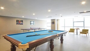 A pool table with balls, a table tennis table, and two chairs in a room with large windows.