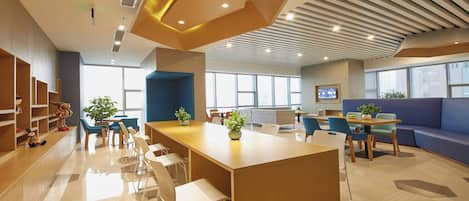 A modern hotel lobby with a central bar area, seating arrangements, and a television screen.