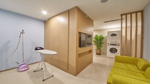 Un salon moderne avec un meuble en bois, un téléviseur à écran plat, un lave-linge et un fauteuil jaune.