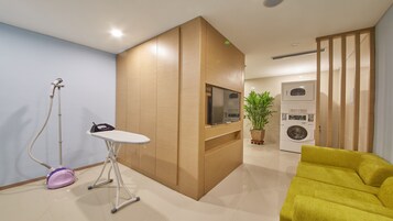 A modern living room with a wooden cabinet, a flat-screen TV, a washing machine, and a yellow armchair.