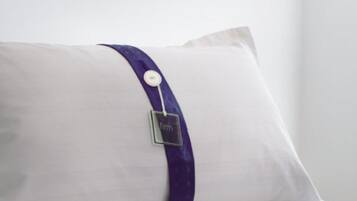 Almohada blanca con una banda morada y una etiqueta metálica.