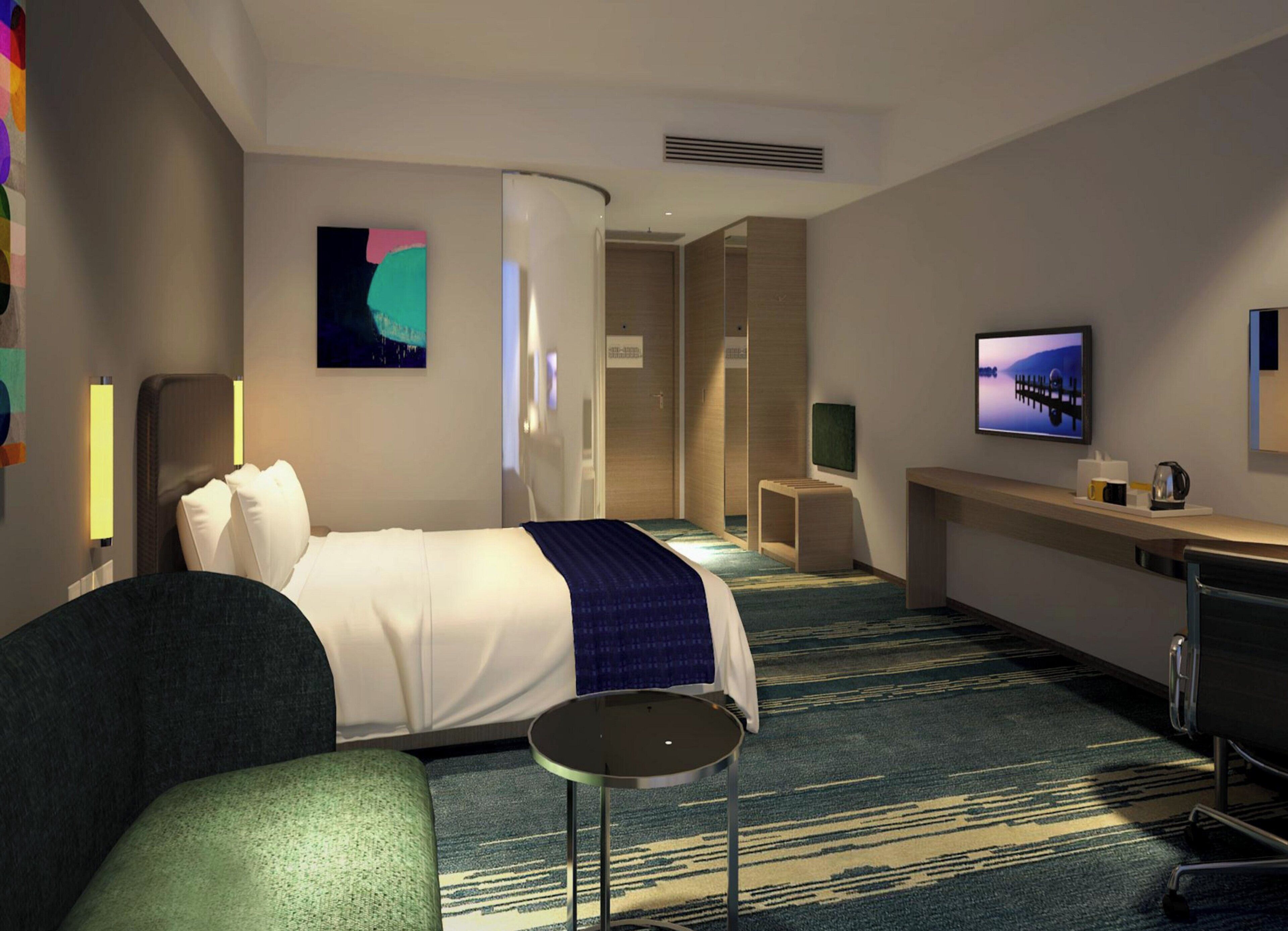A hotel room with a bed, a desk, a chair, a small table, a television, and artwork on the walls.