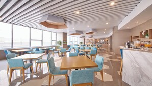 A modern dining area with tables and chairs, a kitchen area, and a bar counter with various food items.