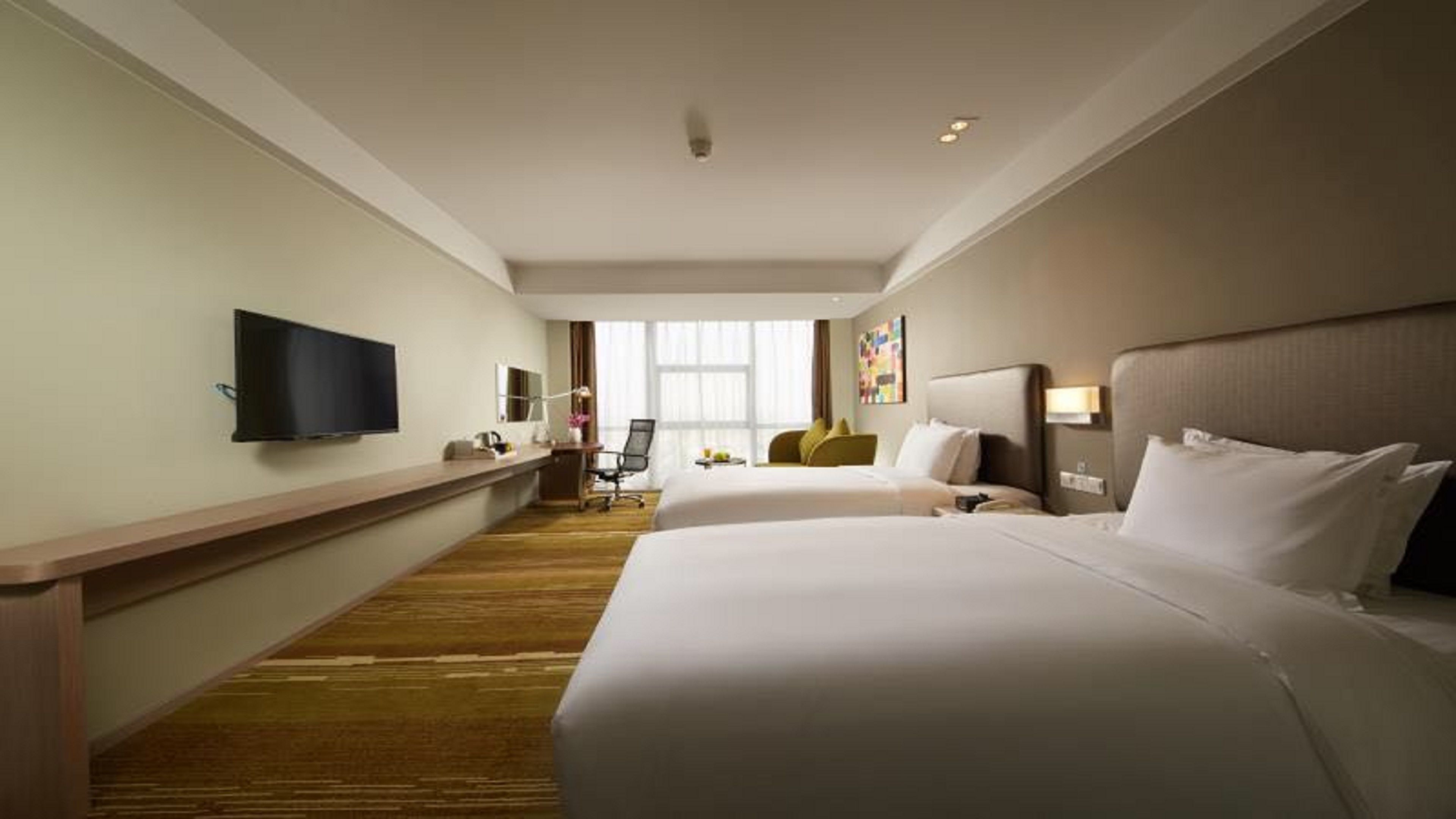 A hotel room with two beds, a TV, a desk, and a window.