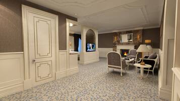 Habitación de hotel con alfombra estampada, televisor, chimenea y una zona de estar con sillas y una mesa.