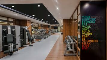 Un gimnasio moderno con diversos equipos de ejercicio, un cartel motivacional y suelo de madera.