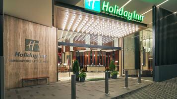 Holiday Inn -hotellin julkisivu Singaporen Little Indiassa: siinä on suuri kyltti, hyvin valaistu sisäänkäynti ja oleskelualue, jossa on ruukkukasveja.