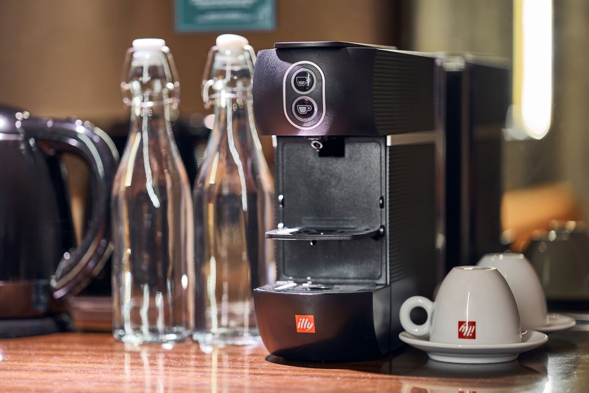 Una cafetera, un hervidor y dos botellas de vidrio sobre una superficie de madera.