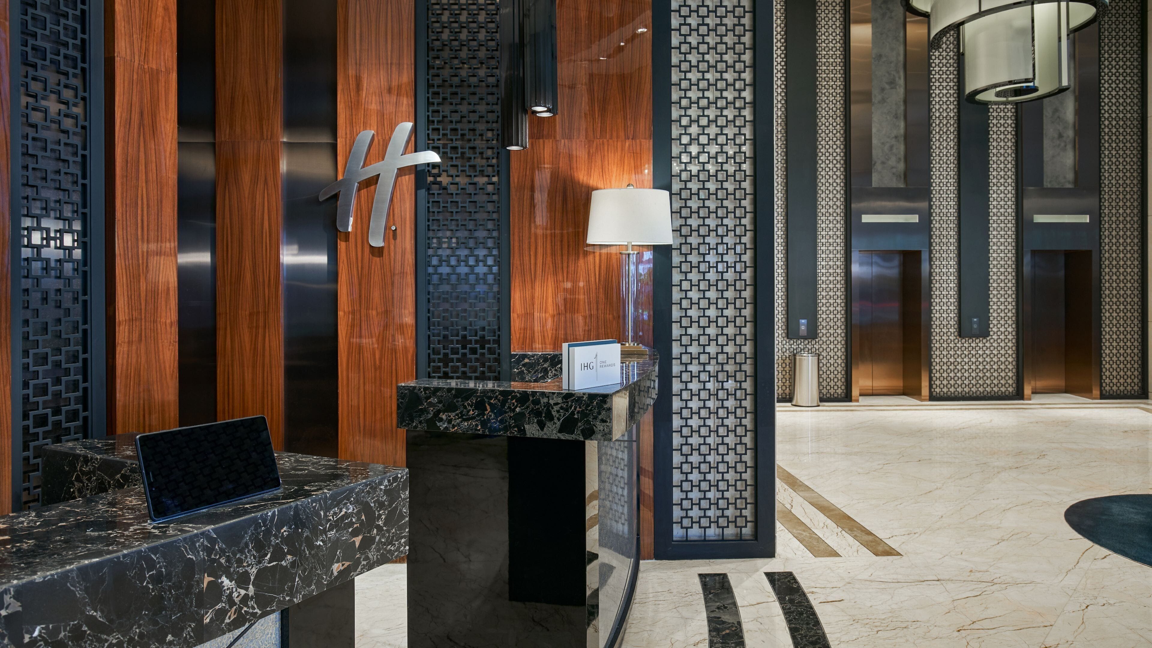 A modern reception desk with a marble top, a laptop, and a sign indicating 'IHG One Rewards'.