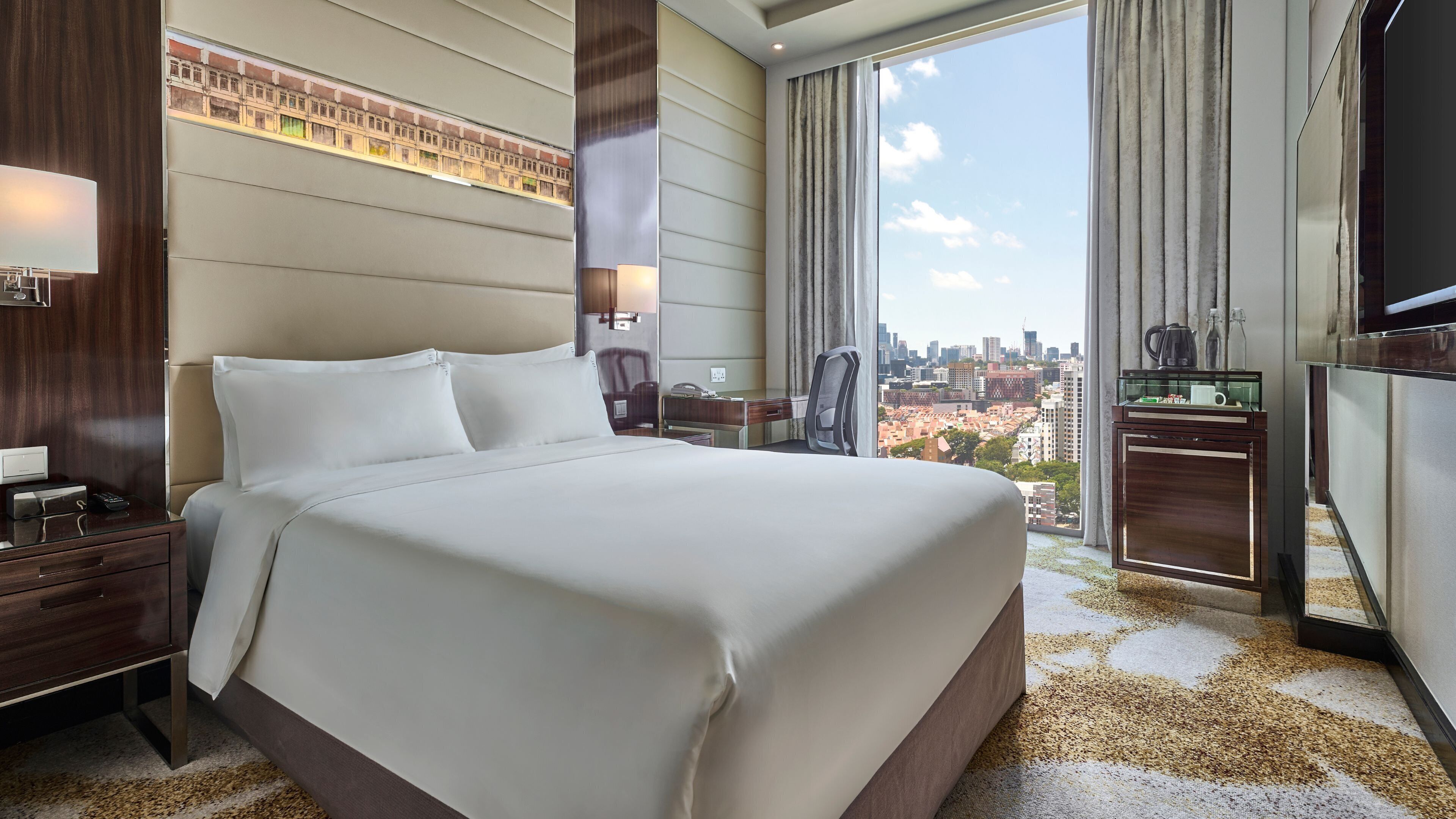 A hotel room with a large bed, a desk, a chair, a TV, and a city view.