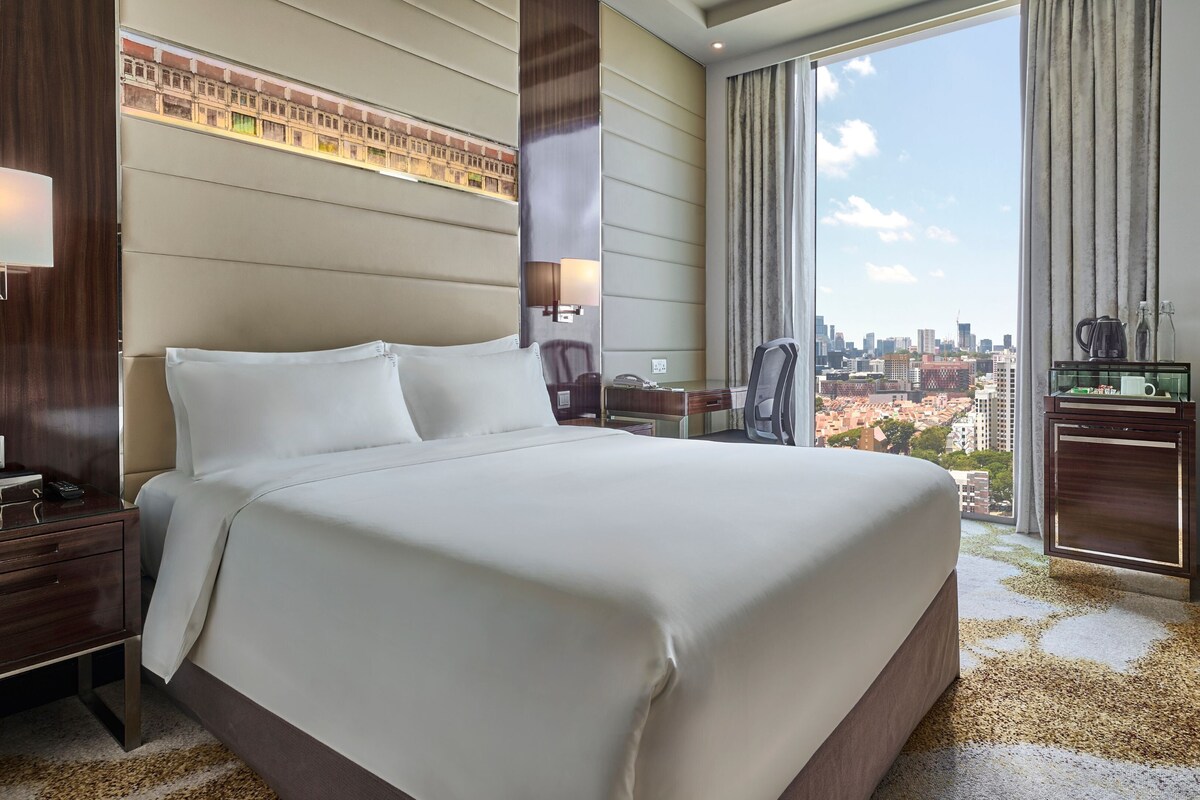 Una habitación de hotel con una cama grande, un escritorio, una silla, un televisor y vistas a la ciudad.