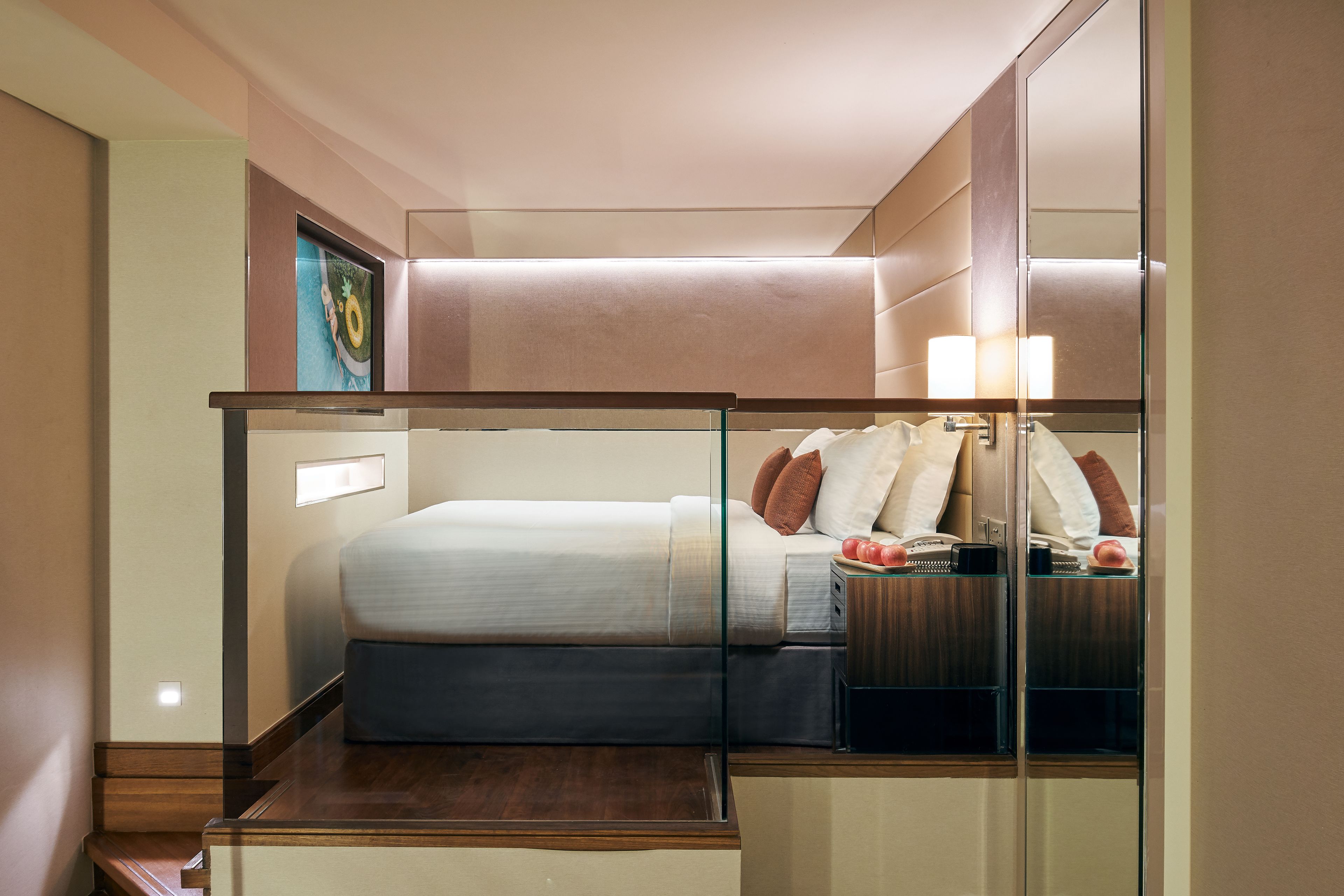 A modern hotel room with a bed, bedside table, lamp, and a large mirror.