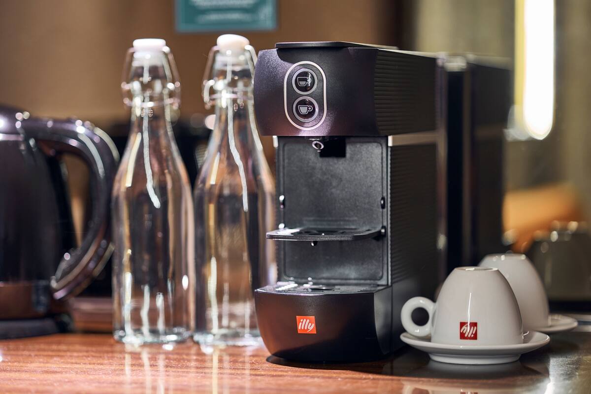 Una cafetera, un hervidor y dos botellas de vidrio sobre una superficie de madera.