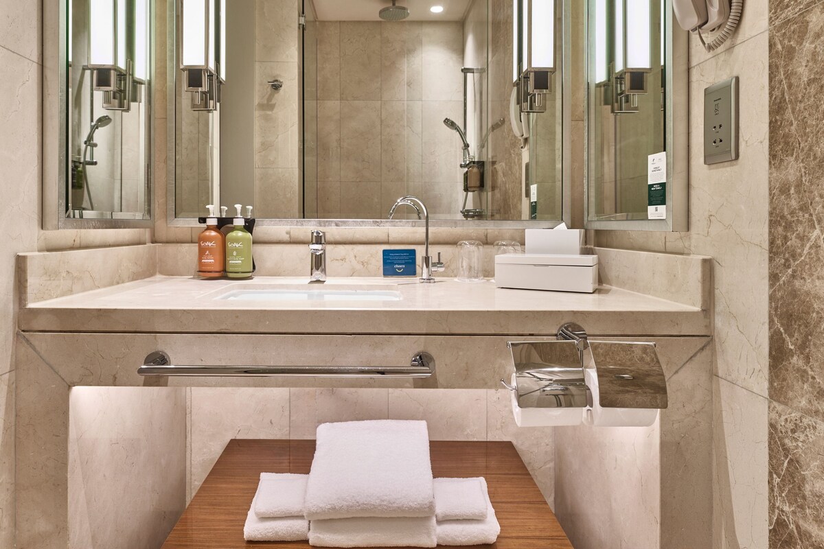 Un baño moderno con un espejo grande, un lavabo, una ducha y un perchero para toallas.